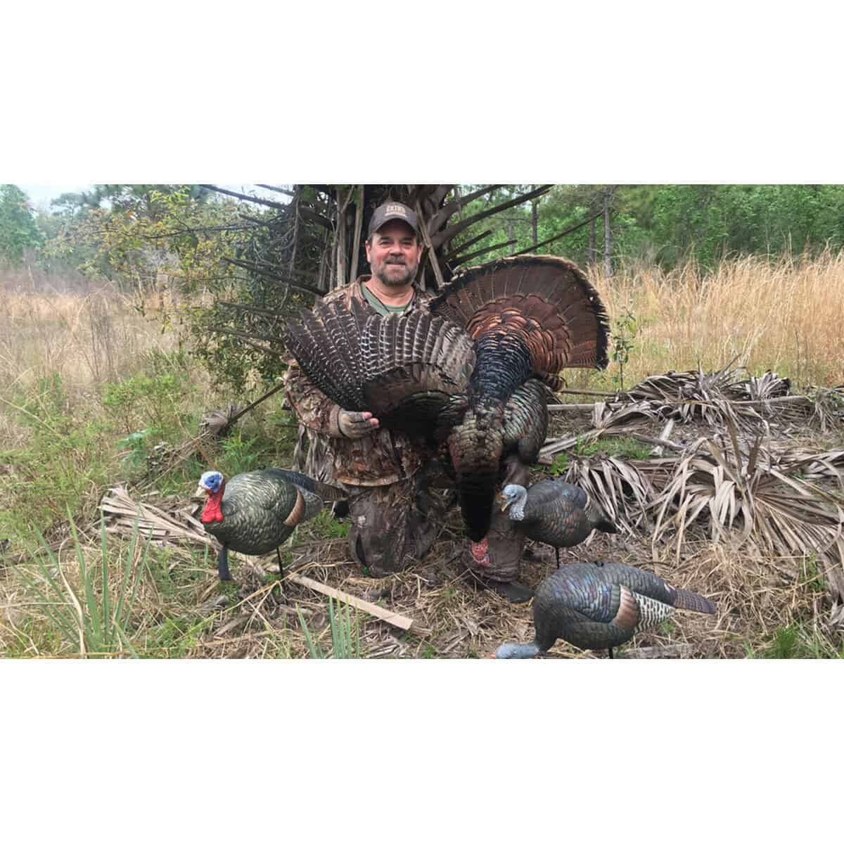 man holding dead turkey with decoys